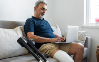 Man with cast sitting on sofa using laptop, slip and fall attorneys Saint Paul MN